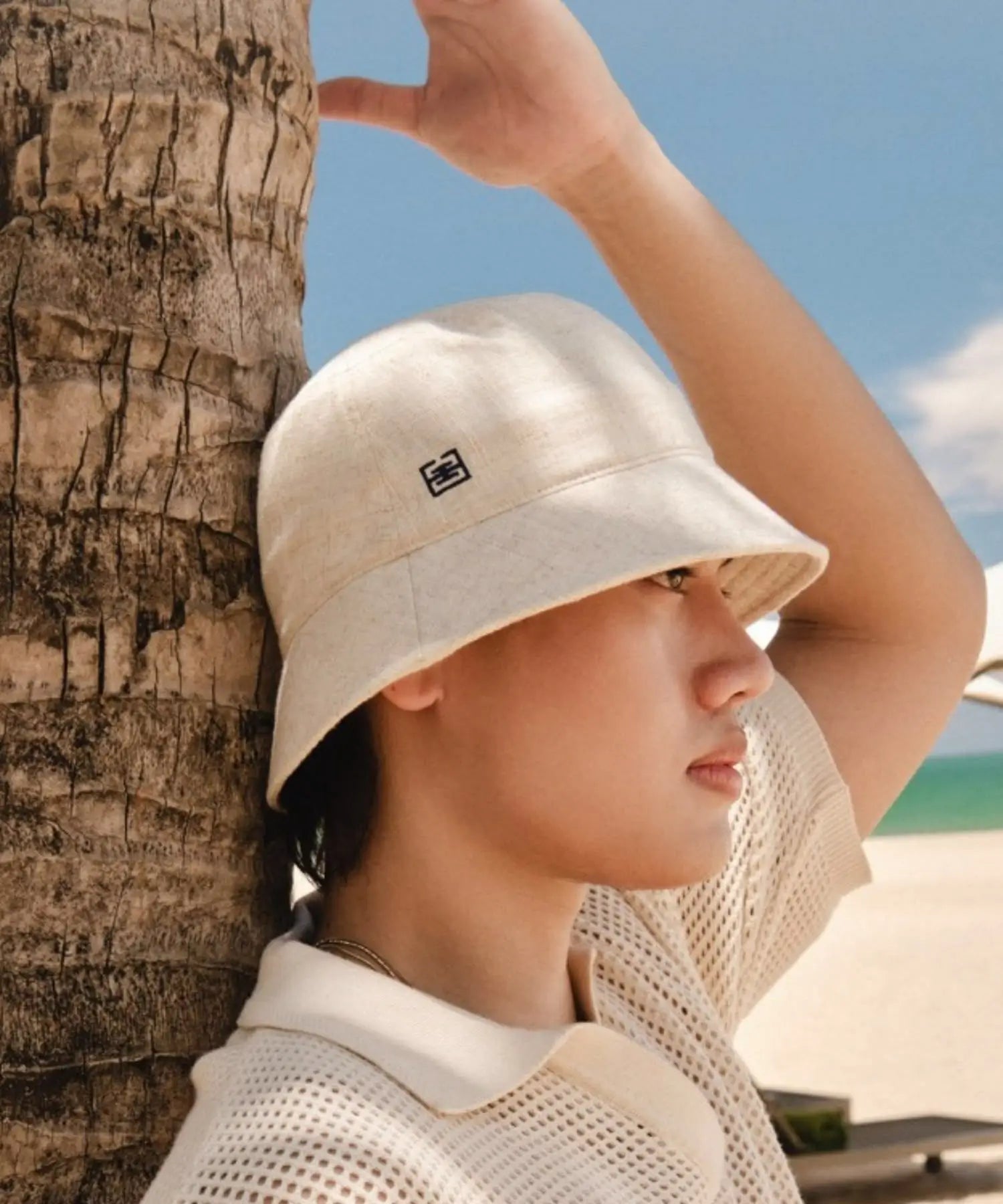 Person wearing a beige bucket hat against a palm tree and blue sky.