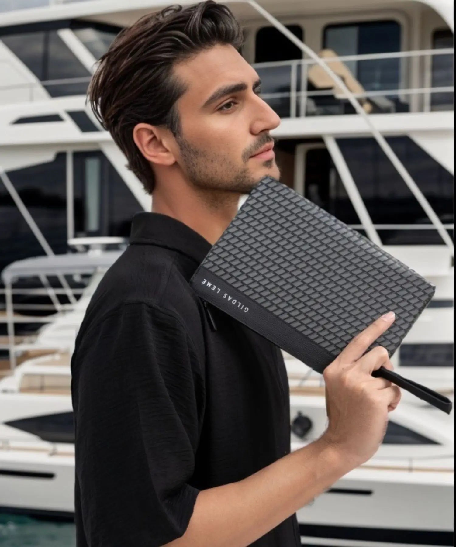 Man holding a textured black clutch with a boat in the background