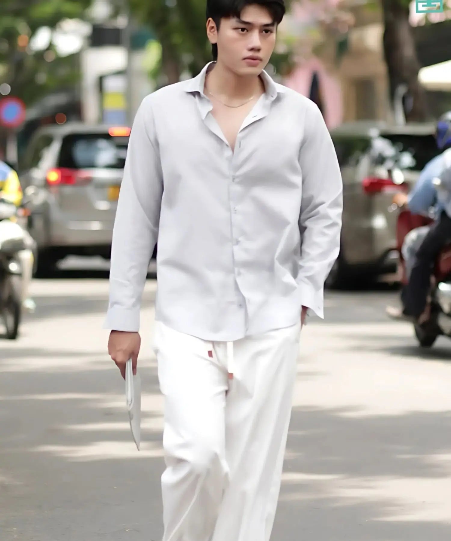 Person wearing a light gray shirt and white pants on a street.