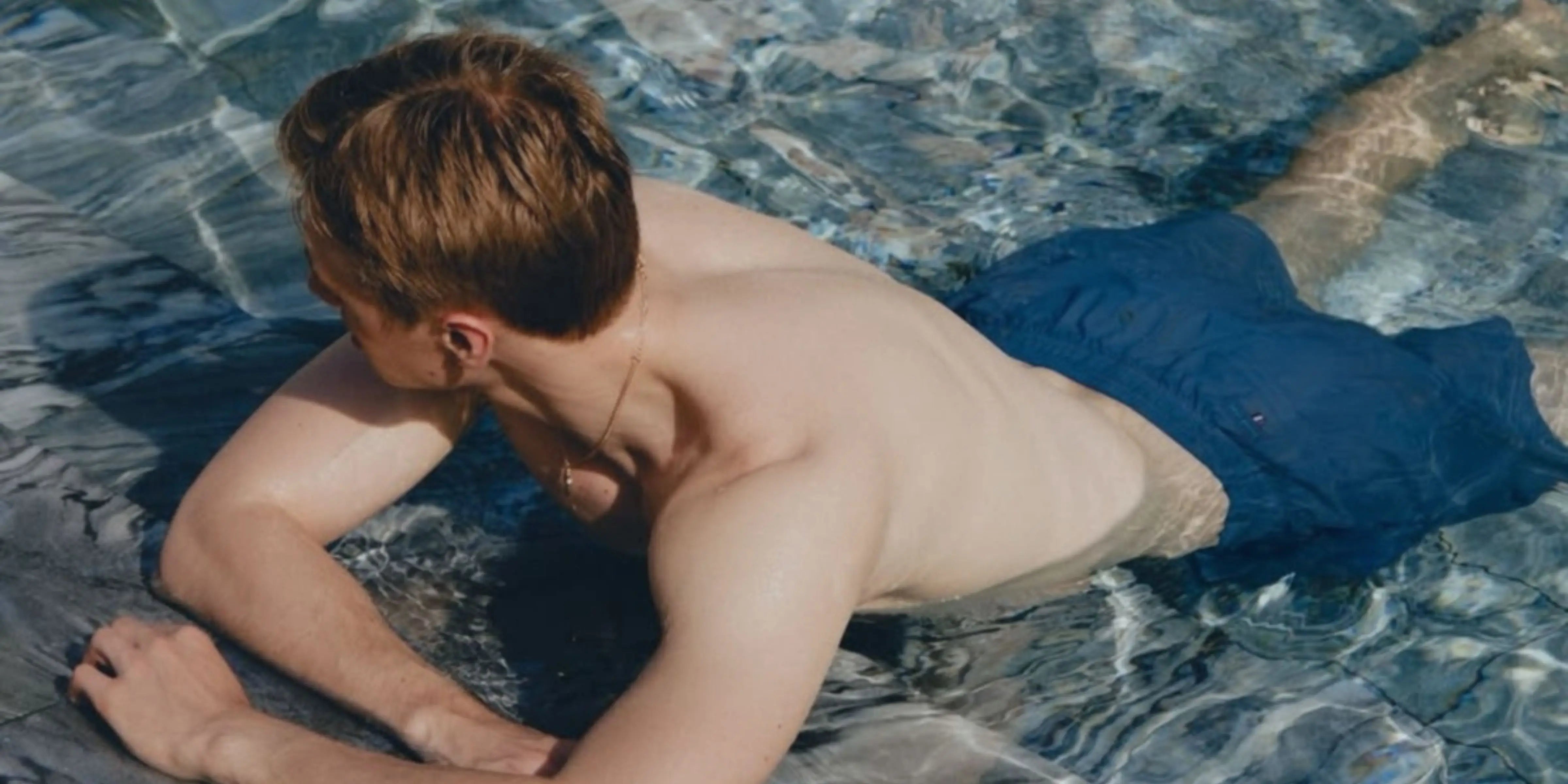 Young boy lying on a towel in a pool wearing blue shorts.