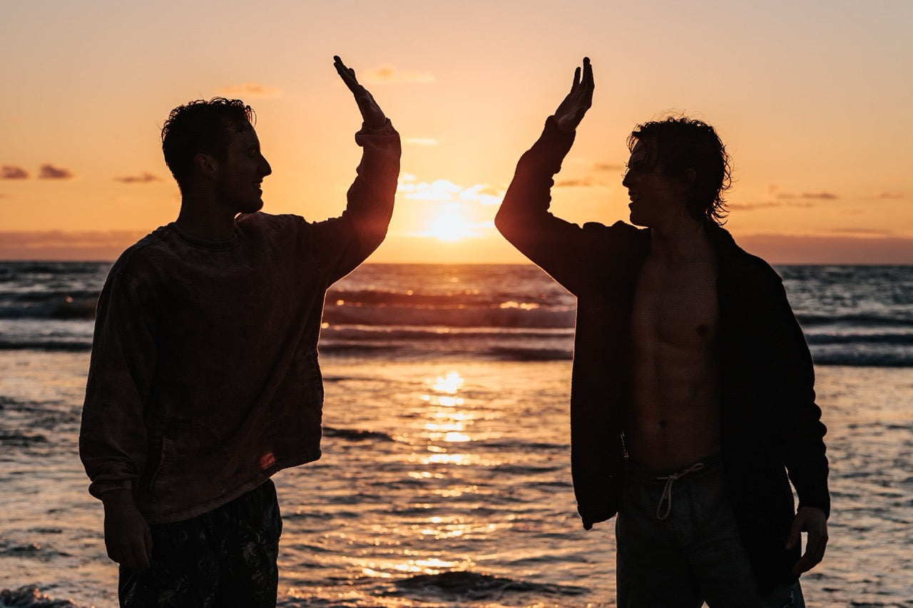Two people standing on a beach at sunset, silhouetted against the ocean.