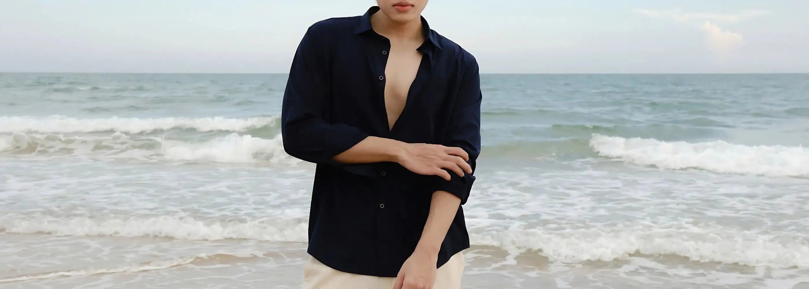 Person wearing a black shirt with open collar standing on a beach