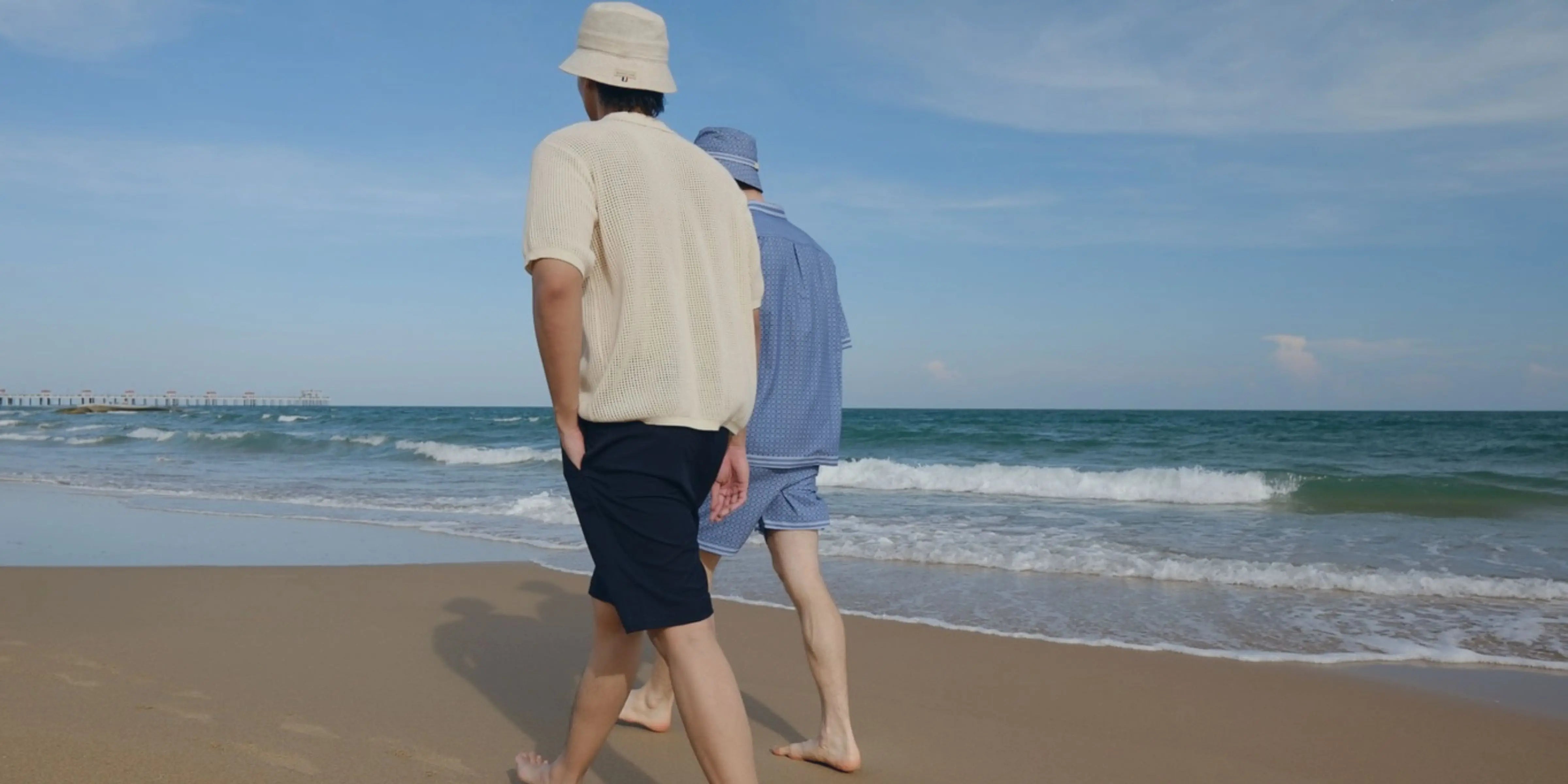 Two people walking on a beach with ocean waves and clear sky.
